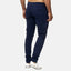 Ein Mann steht mit dem Rücken zur Wand und trägt eine Elara Slim Fit Chino-Hose in Marineblau für optimalen Komfort, dazu weiße Sneakers mit schwarzen und roten Akzenten vor einem schlichten hellgrauen Hintergrund.