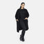 Eine Frau präsentiert einen lässigen Look in einem übergroßen Elara-Cardigan für maximalen Komfort, kombiniert mit einem schwarzen Top, Leggings und Schnürstiefeln. Sie steht vor einem weißen Hintergrund, hat die Hände in den Taschen und lächelt leicht.