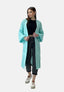 Eine Frau in einem langen hellblauen Oversize-Cardigan von Elara, einem schwarzen bauchfreien Top, dunklen hochgekrempelten Jeans und weißen Turnschuhen steht vor einem schlichten Hintergrund für einen lässigen Look.